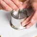 A person using an Ateco stainless steel round mold to shape food.