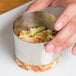 A hand holding a silver metal round mold filled with food.