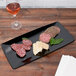 A black GET Siciliano tray with food on a table.