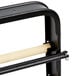 A black metal horizontal countertop paper cutter rack with wooden dowels.