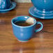 A blue Fiesta china cup with tea in it and a tea bag on a table.