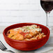 A red Fiesta Bistro bowl filled with spaghetti and meatballs on a table in an Italian restaurant.