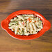 A red Fiesta oval casserole dish filled with pasta and vegetables.