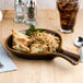 A Tuxton caramel fry pan server filled with rice and chicken on a table with a glass of ice water.