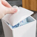 A hand picking up a sugar packet from a white Cal-Mil lid on a counter.