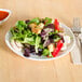 An eggshell ellipse china plate with a salad on it, with a fork and knife.