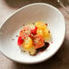 A Tuxton white porcelain bowl filled with tomatoes and sauce on a table.