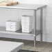 A Regency stainless steel undershelf for a work table with white containers on it.