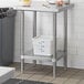 A Regency stainless steel work table with an undershelf holding a white plastic container.