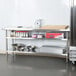 A metal shelf holding bowls and containers underneath a Regency stainless steel work table.