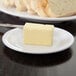 A Carlisle white melamine bread and butter plate with a piece of bread and butter on it.