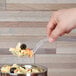 A hand holding a Fineline clear plastic serving spoon full of pasta.