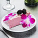 A piece of Tuxton Pacifica china with blackberry cheesecake topped with flowers and berries.