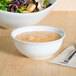 A Tuxton bright white china nappie bowl filled with soup next to a bowl of salad on a table.