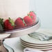 A cake with strawberries on top under a clear dome on a glass cake stand.