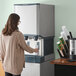 A woman filling a Scotsman countertop water dispenser with ice and water using a white and green cup.