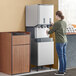 A woman standing next to a Scotsman stainless steel ice and water dispenser stand.