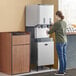 A woman using a Scotsman stainless steel ice dispenser stand with door.