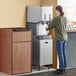 A woman using a Scotsman stainless steel ice dispenser stand with door.