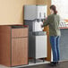 A woman using a Scotsman stainless steel ice dispenser stand to fill a drink.