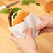 A person holding a burger wrapped in heavy duty dry wax paper.