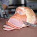 A person using a Waring cordless electric knife to cut ham on a cutting board.