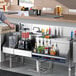 A man standing at a stainless steel Uni-Serv speed bar with a drink in his hand.