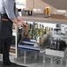 A man in an apron placing bottles of alcohol on an Advance Tabco Prestige Series stainless steel liquor display rack.
