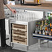 A man standing next to an Advance Tabco stainless steel glass rack storage cabinet with a tray of drinks on the counter.