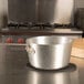 An American Metalcraft black silicone oval trivet holding a metal pot on a table.