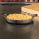 An American Metalcraft black oval silicone trivet under a pan of macaroni and cheese.