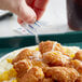 A hand pouring salt onto a plate of food.