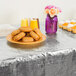 A table with a silver metallic plastic table cover, a plate of doughnuts, and a vase of flowers.