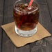 A glass of iced coffee with a straw on a table with a Creative Converting Glittering Gold beverage napkin.