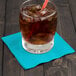 A glass of iced coffee with a straw and a Bermuda Blue 2-ply beverage napkin on a table.