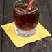 A glass with ice and a straw on a yellow Creative Converting beverage napkin.