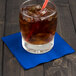 A glass with ice and a straw on a Cobalt blue beverage napkin.