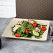 A plate of salad with tomatoes, cucumbers, mushrooms, and spinach on a Papyrus-colored square plate.