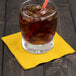 A glass with ice and a yellow School Bus beverage napkin on a table.