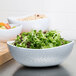 A white Coralline melamine triangle bowl filled with salad, lettuce, and fruit.