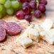 A rectangular marble counter with a cheese and meat platter, salami, and grapes on white Elite Global Solutions rustic granite trays.
