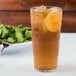 A clear plastic tumbler of iced tea with a lemon slice on the rim.