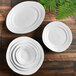 A group of white irregular round bowls with a leaf and fern design on a wooden surface.