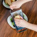 A person grating cheese on a plate with a Tablecraft flat grater.