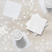 A stack of white Creative Converting 3-ply beverage napkins on a wooden table.