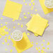 A table with yellow Creative Converting Mimosa Yellow beverage napkins and cups of liquid.