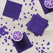 A purple Creative Converting beverage napkin on a table with a cup of purple liquid.