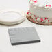 A white table with a white cake and a stack of Shimmering Silver napkins.