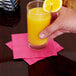 A person holding a glass of hot magenta pink Creative Converting beverage napkin with a slice of lemon on a table.