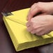A person wrapping a Creative Converting Mimosa Yellow luncheon napkin around a fork and spoon.